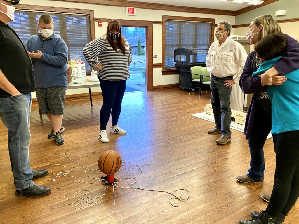 Participants standing around a basketball balanced on a cup.