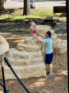 Toddler climbing on an outdoor play structure with dad standing close by