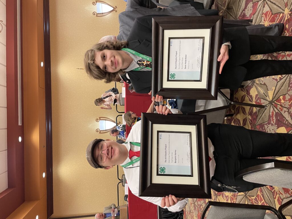 Two well dressed teenagers pose with awards in frames.