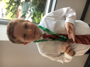 A young boy in a formal shirt and tie wearing a green lanyard.